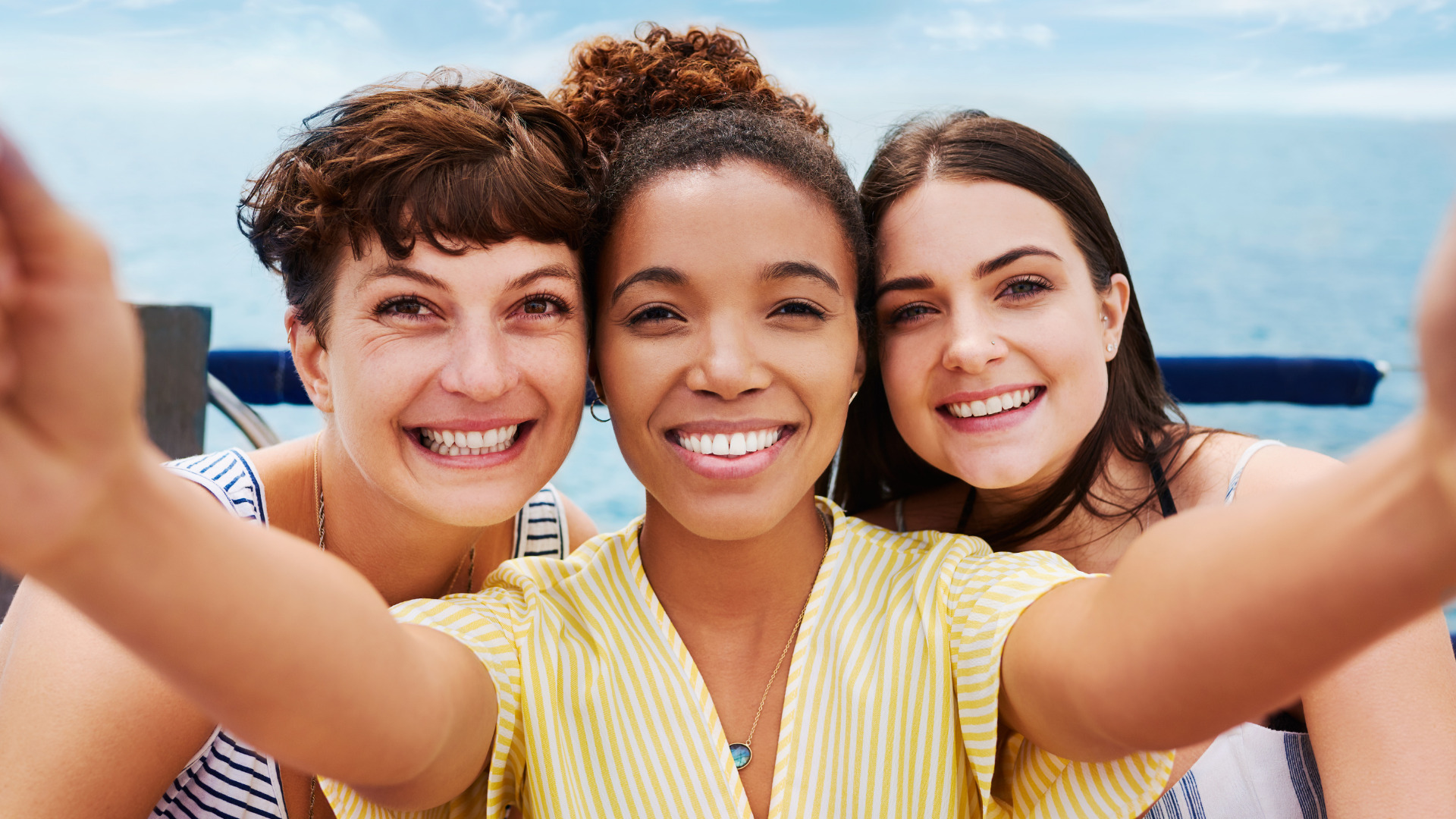Three women smiling and posing for a selfie on a boat, capturing a joyful moment together.