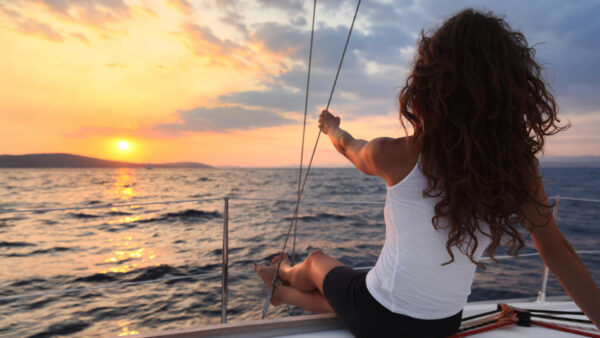 A woman enjoying the sunset on a sailboat's bow.